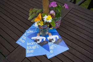 u3a flyers which show a woman dancing and the words, 'learn, laugh, live' on a table with flowers in jam jars