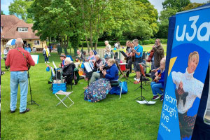 People sitting outside next to a big u3a poster 