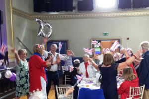 A group of people waving union jack flags with a silver 70 balloon in the background