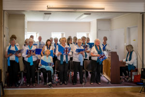 A choir of people singing from blue books with a union jack on the front cover