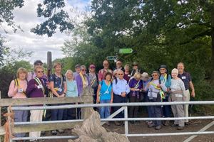 A large group of older adults standing on a walking path, behind a field gate