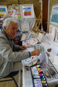 A man is painting on a table covered with artistic materials