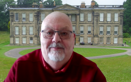 a man in a red jumper smiling with glasses and grey hair and beard