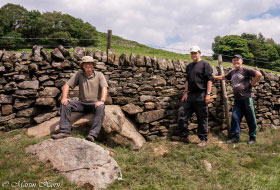 three men standing in front of a stone wall