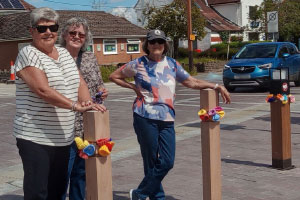 group of three women standing next to bollards with knitted flowers on