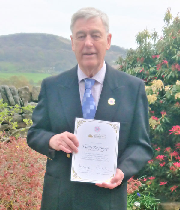 A man in a suit standing outside holding a certificate that says Coronation Champion Harry Roy Biggs