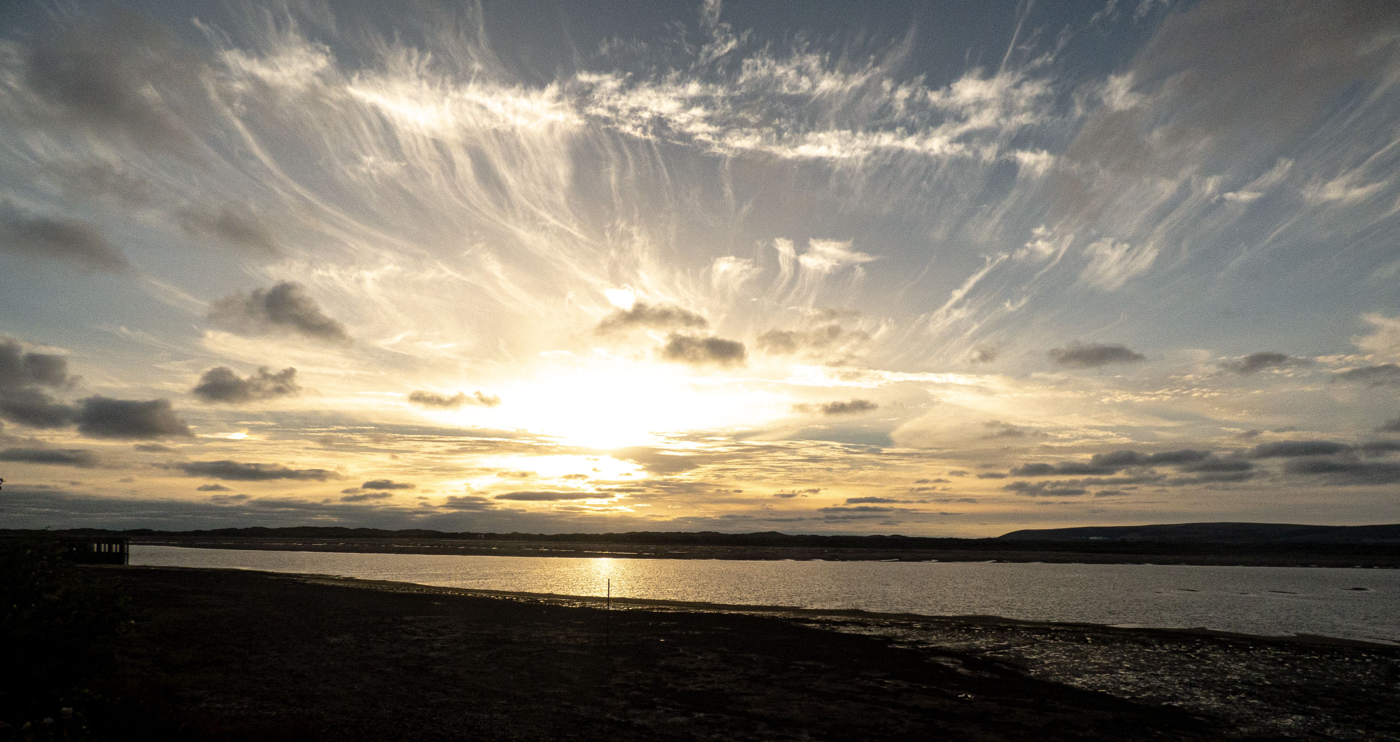 clouds streaming out of the sun which is setting over sea. 