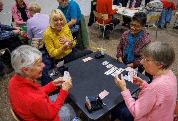 4 people around a table playing cards and smiling
