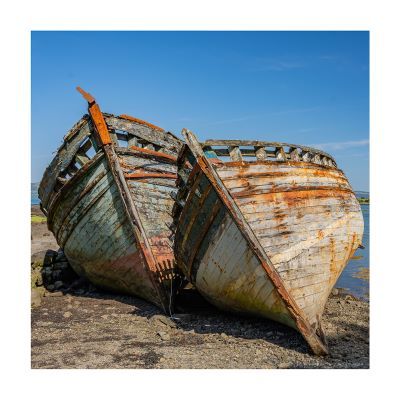 two rusting boats leaning against each other in the sunshine