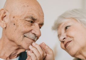an older man and woman looking at each other holding hands
