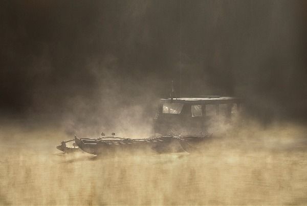 A boat heavily shrouded in brown mist, the whole image has a brown / tan hue