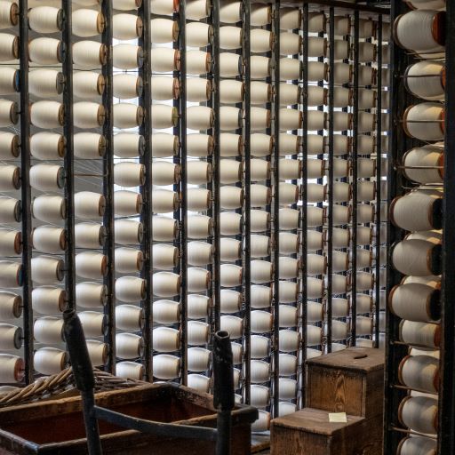 a wall of large bobbins with white thread on. Dark wooden structure holds up the bobbins.