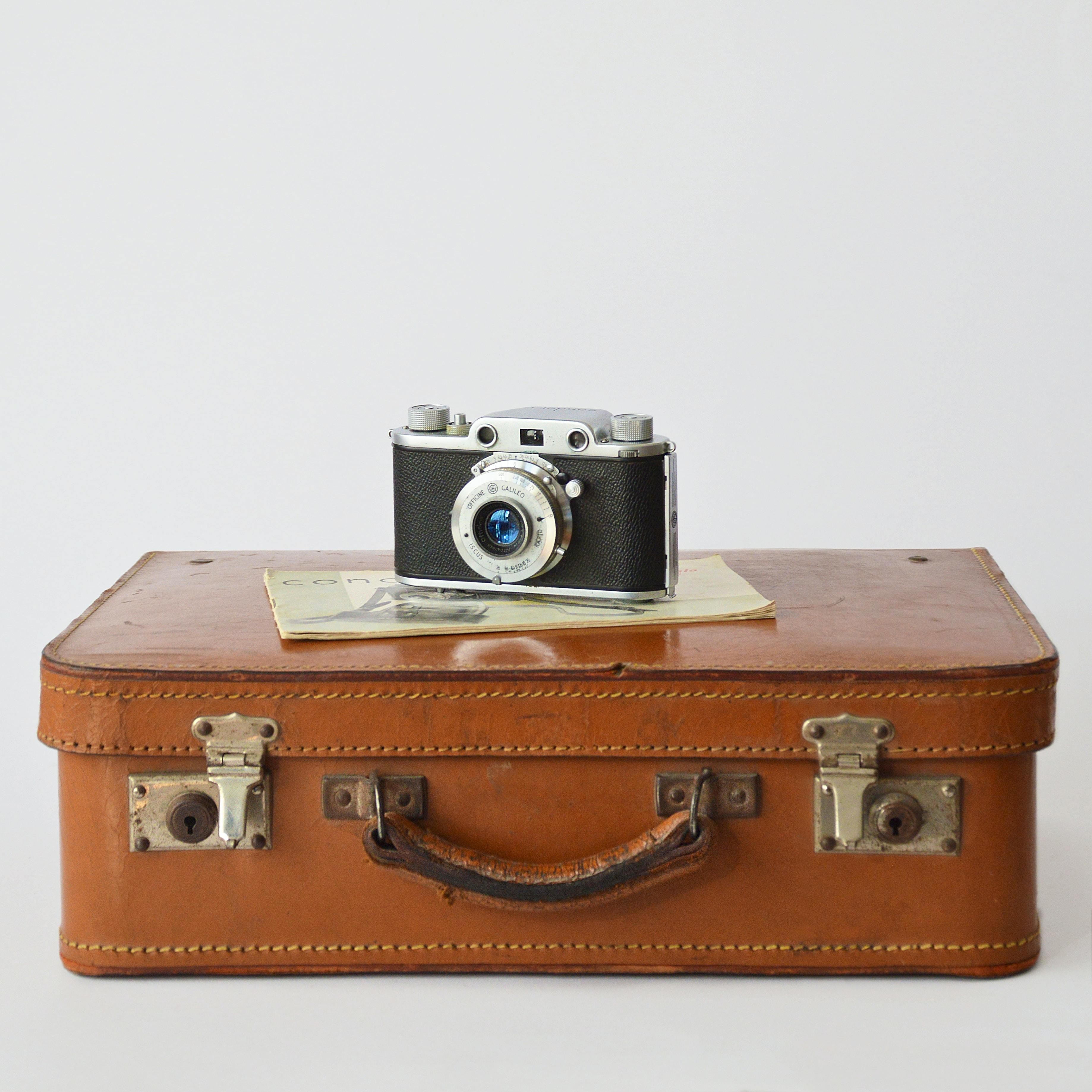 an old fashioned brown leather suitcase with an old camera on top of it