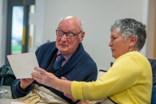 a man in a tie being shown a piece of paper by a woman in a yellow cardigan