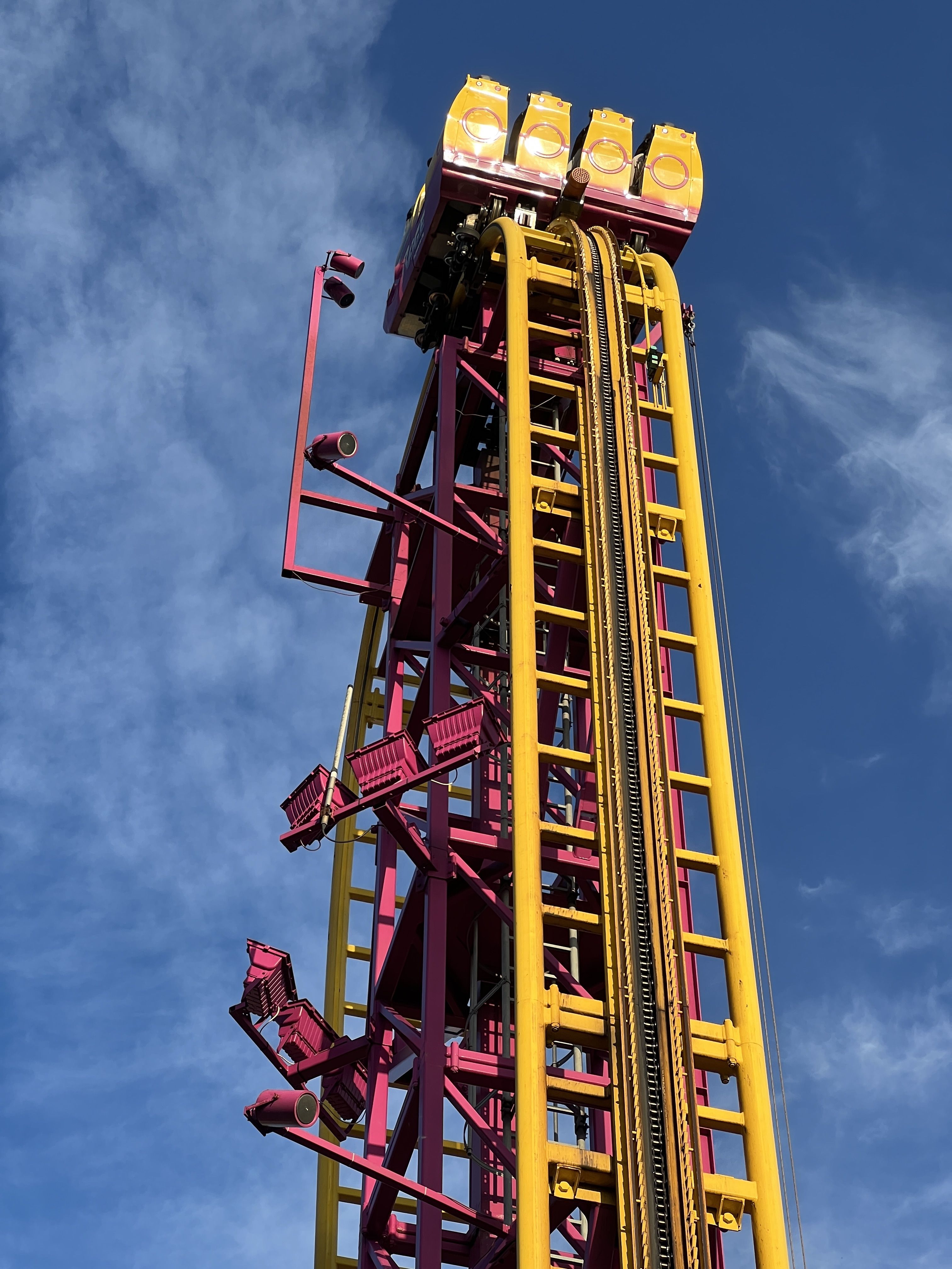 looking up at a yellow and pink rollercoaster with sunny blue sky behind