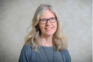 A blonde woman in a grey top, Sam Mauger, smiling at the camera