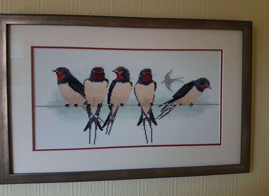 a cross stitch artwork of 5 swallows on a wire