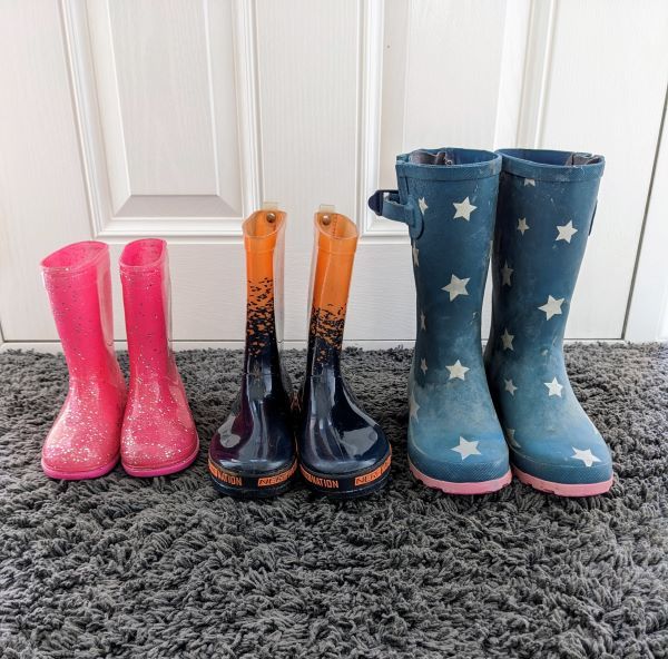 three pairs of wellington boots lined up side by side. Pink ones are small, orange and black ones are bigger, navy blue with white stars are biggest. 