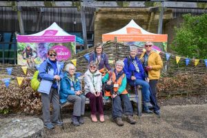 Eight women standing in front of a wall that has blue and yellow u3a bunting on it. They are all smiling.