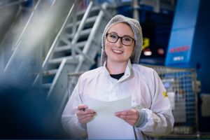 A woman in a white apron and white net covering her hair is holding pieces of paper and standing in a space station