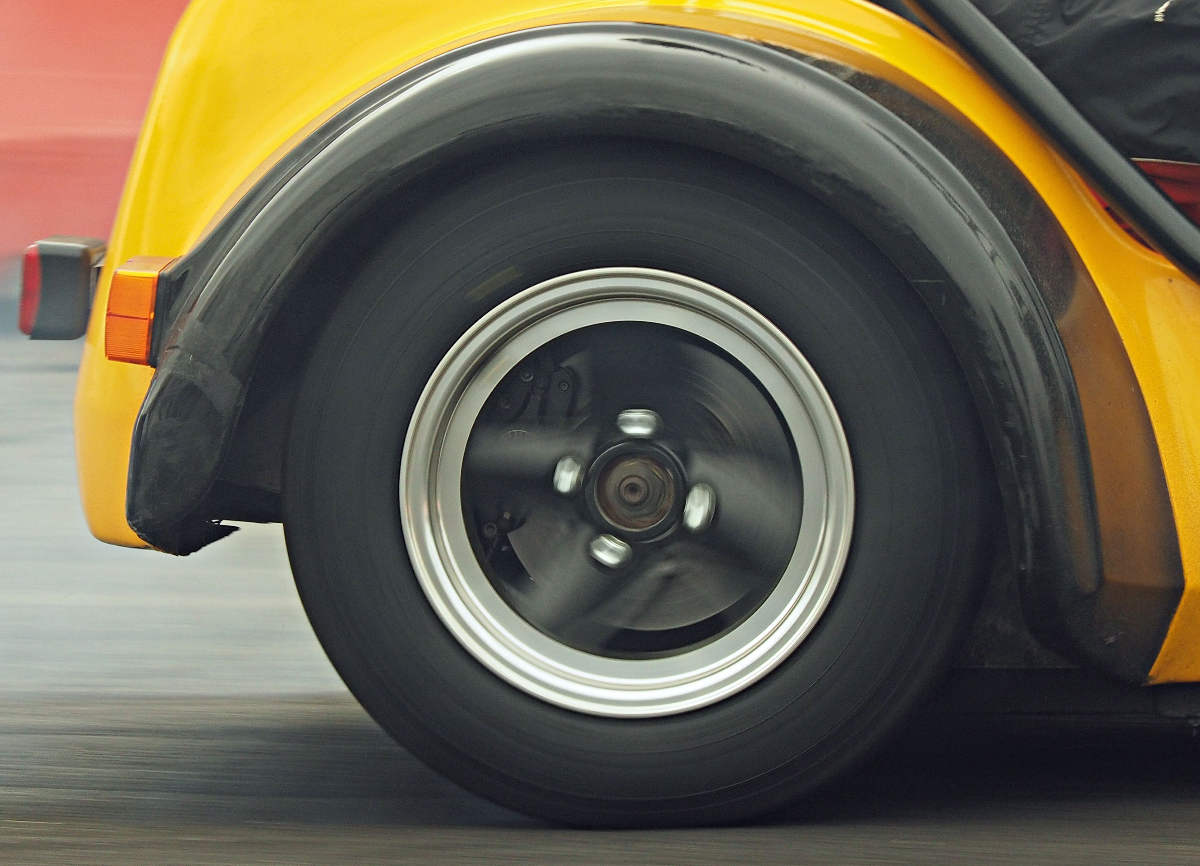 a car wheel on the road moving. the car is yellow.