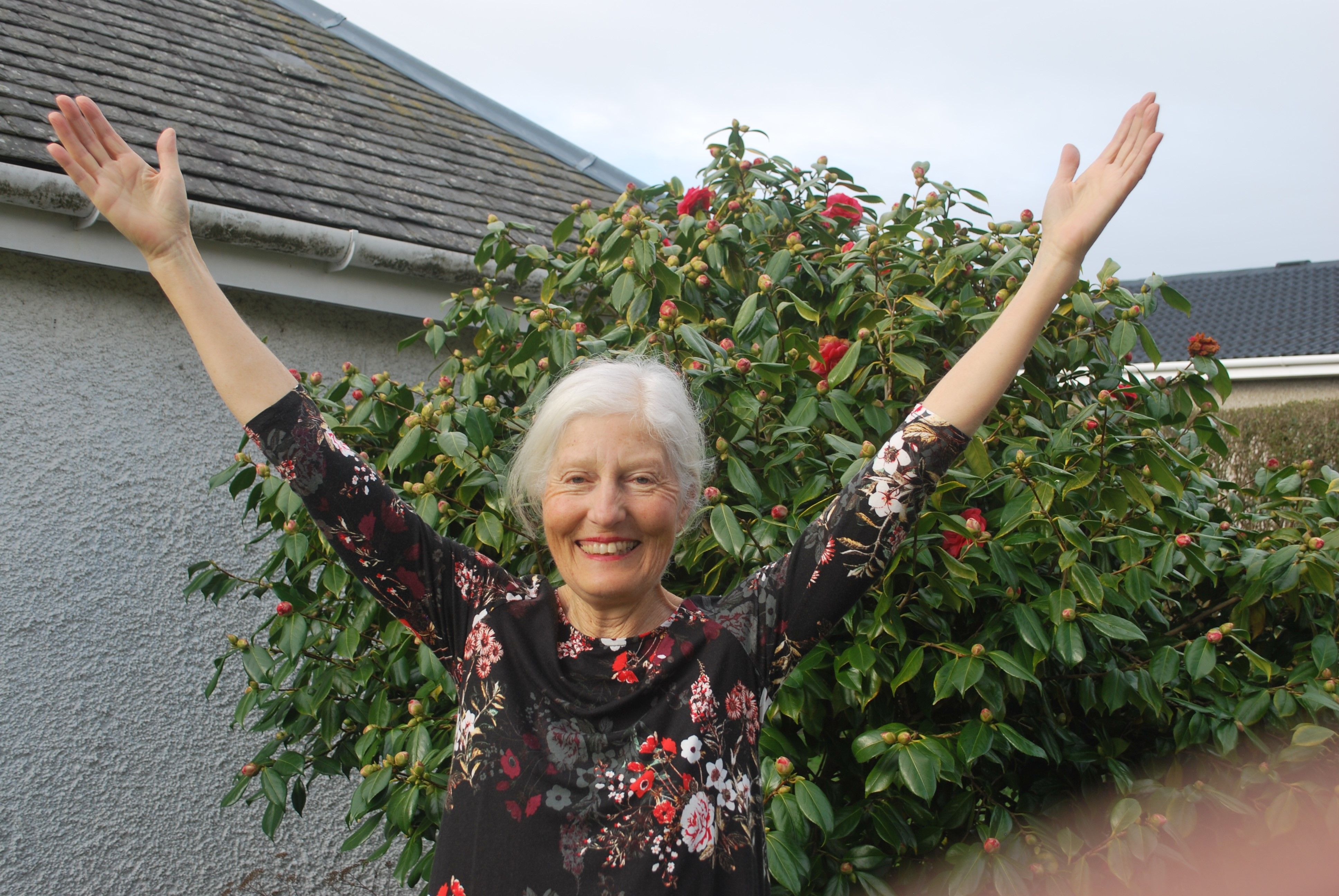 a woman in a floral top with her arms in the air smiling 